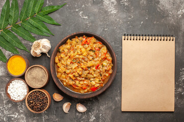 top view roasted eggplant salad in bowl garlic different spices in small bowls notepad on dark background