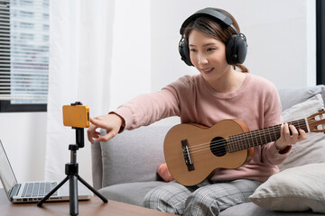 Asian woman sitting at living room playing guitar, Music blogger concept.