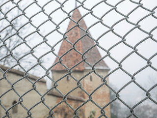 Fototapeta premium Wire fence covered with hoarfrost or rime ice on a misty morning with a old medieval tower in the background.