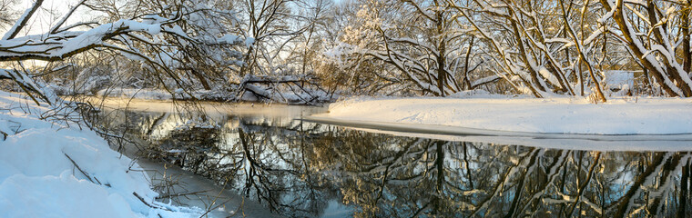 Frosty winter scene with forest river on a sunny morning. Beautiful snow covered trees in the glow of rising sun. 