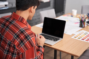 Designer wearing plaid shirt working on laptop - obrazy, fototapety, plakaty