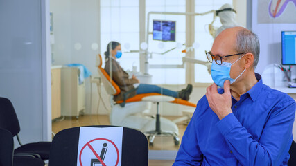 Portrait of elderly patient with protection mask talking sitting on chairs keeping social distance...