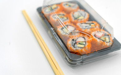 Food delivery, Sushi rolls ready to eat in plastic container with chopsticks, image on white background.