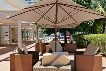 A large open clear parasol. Several empty pool chairs. In the background, deck and vegetation.