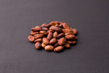 Unpeeled raw brown cocoa beans in heap lie On black modern concrete background. Flat lay, mock up, copy space. Raw materials for making cocoa powder, cocoa beverages, chocolate. Health drink concept