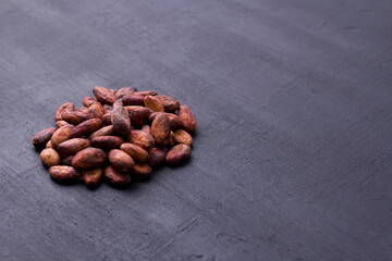 Unpeeled raw brown cocoa beans in heap lie On black modern concrete background. Flat lay, mock up, copy space. Raw materials for making cocoa powder, cocoa beverages, chocolate. Health drink concept