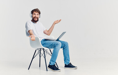 man in headphones with laptop on his knees sitting on chair communication isolated background