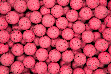 Small, sweet pink balls. Round boilies used as carp fishing bait. Abstract pink background