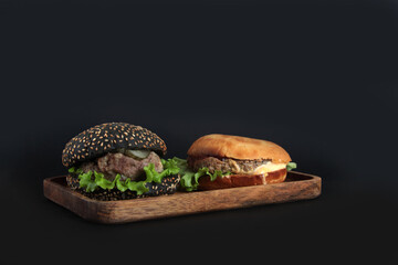 two hamburgers on wooden plate isolated on black background