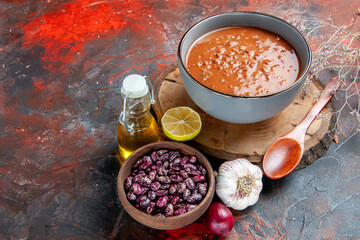 Deliciou soup for dinner with a spoon and lemon on a wooden tray beans garlic onion and oil bottle on mixed color background