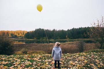 a little girl stands with her back to the autumn park and holds a balloon in her hand 