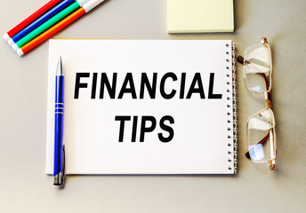 FINANCIAL TIPS . blank notebook with markers pen beside. The notebook is on paper with text . Colored pencils and eyeglasses. Concept photo.