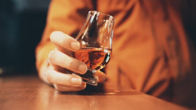 Color close up shot of a person holding a Glencairn whisky glass on a wooden table, with shallow depth of field.