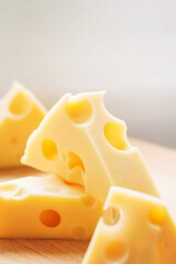 Swiss yellow cheese triangular chunks with holes on wooden plate. Maasdam Dutch cow's milk cheese.