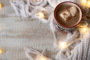 Hot cocoa with marshmallow in a ceramic christmas mug surrounded by winter things on a wooden table. Space for text.