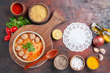 Horizontal view of tomato meatballs soup with noodles in a brown bowl and different spices oil bottle onion garlic and napkin on dark background