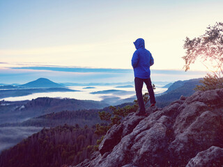 Hiker in blue jacket has hands in pocket. Hiking in sunrise. Man hiking in sunset in mountain