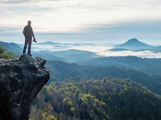 Camera in the hand of tourist standing on rock. Photographer hold camera within autumnal day.