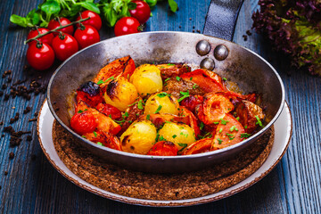 Roasted cherry tomatoes in cast iron skillet on wooden table.