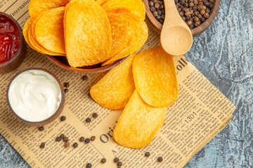 Close up view of delicious homemade chips and pepper bowl mayonnaise ketchup with spoon on newspaper on gray table