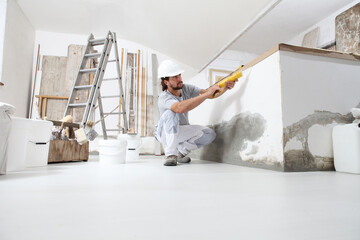 construction worker plasterer man uses caulking gun in building site of home renovation with tools...