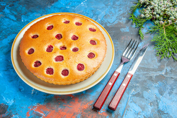 front view raspberry cake on oval plate cones fork knife on blue table