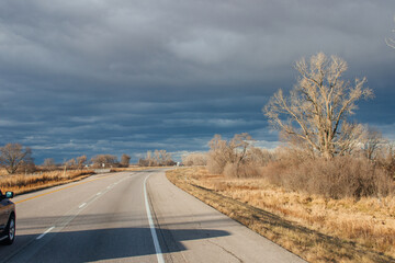 Beautiful dark blue sky over the highway. A landscape with a very unusual sky, trees without leaves and an asphalt road on an autumn day before a thunderstorm. Pacific Junction, IA, USA, 11-30-2019