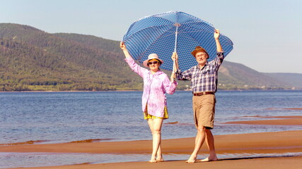 Happy and mature couple in love walk along the sandy bank of the river on a summer sunny day against the background of mountains