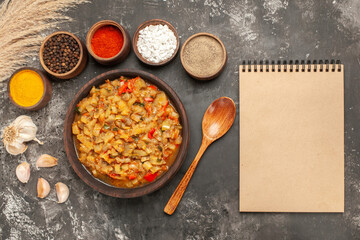 top view roasted eggplant salad in bowl different spices in bowls garlic notebook on dark background