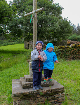 Senderismo en el Camino de Santiago. Dos ni&ntilde;os descansan al pi&eacute; de un cruceiro un d&iacute;a de lluvia
