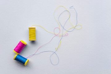 Isolated spools of colored plastic threads, scattered threads on the floor. Blue pink and yellow thread.  
Colored threads used for sewing. Top view.