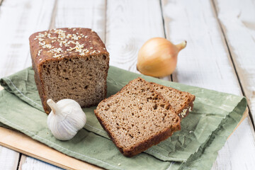 Freshly baked sourdough bread made from rye flour on a green linen napkin. Slices of bread, onion and garlic.