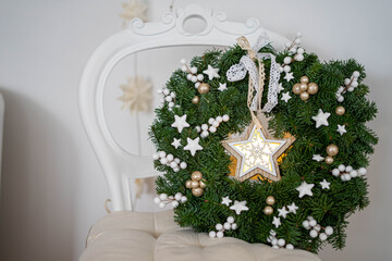 Christmas wreath made of 
spruce branches together with a lighting star. Interior decoration for christmas time.