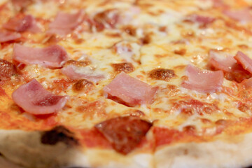 Sliced cheesy pizza on wooden cutting board.Delicious Italian food delivered in cardboard box for lunch meal.Crusty thin dough baked in oven with tasty parmesan,gorgonzola,mozzarella,ham and cheese