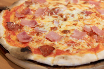 Sliced cheesy pizza on wooden cutting board.Delicious Italian food delivered in cardboard box for lunch meal.Crusty thin dough baked in oven with tasty parmesan,gorgonzola,mozzarella,ham and cheese