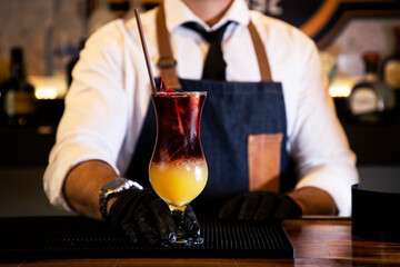 Detail of the hands of a bartender with black gloves placing a crystal glass with a cocktail inside, on a bar counter