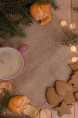Fototapeta na wymiar Home Christmas comfort, pink cup with coffee next to a branch of a christmas tree with tangerine and gingerbread on a wooden table, christmas table with coffee, happy new year time