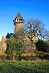 Panoramic view over moat on medieval water castle and defensive tower with bare trees in winter against blue sky - Krefeld Linn