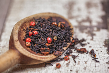 Loose tea leaves with dried berries on a vintage wooden spoon and table