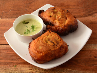 Aloo pakora or aloo bhajji served with chutney, a famous midday snack in india, served over a rustic wooden background, selective focus