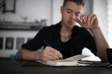 Serious man smoking cigarette while writing at notebook at table