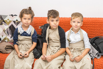 Three children sit in aprons on a red sofa and look at the camera