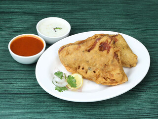 Bread pakora or pakoda served with chutney, a famous midday snack in india, served in white plate, selective focus