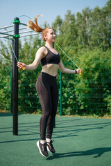 Attractive female jumping rope on athletic field. Fitness cardio training with rope raising dust working out legs.