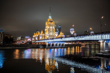 Fototapeta na wymiar evening winter cityscape with river bridge and illuminated buildings