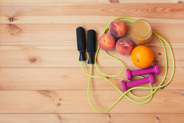 Pink dumbbells, jumping rope, fresh fruits and homemade healthy fruits smoothie made of oranges,...