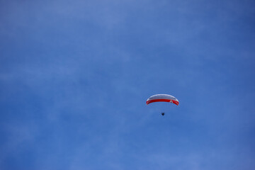 single red white paraglider with blue sky