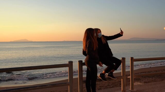 Two Young Girls Taking A Selfie During golden Hour At The Beach In Winter