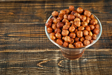 Hazelnuts in a transparent glass bowl on an old shabby board. Nuts on a brown wooden table.