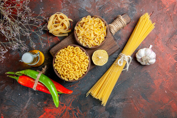 Side view of uncooked pastas on cutting board cayenne peppers tied in one another with rope oil...